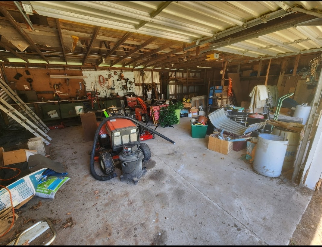 Garage before the cleanout, packed with a riding mower, shop vacuum, ladders, bins and scattered belongings.